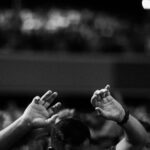 A black and white photo of hands raised in a crowd during a concert or religious gathering indoors.
