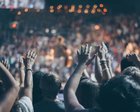Energetic crowd at a live concert with hands raised and bright lights.