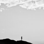 Black and white silhouette of a person standing on a mountain under a cloudy sky.