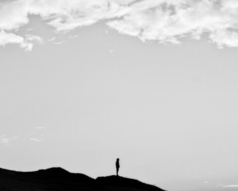 Black and white silhouette of a person standing on a mountain under a cloudy sky.