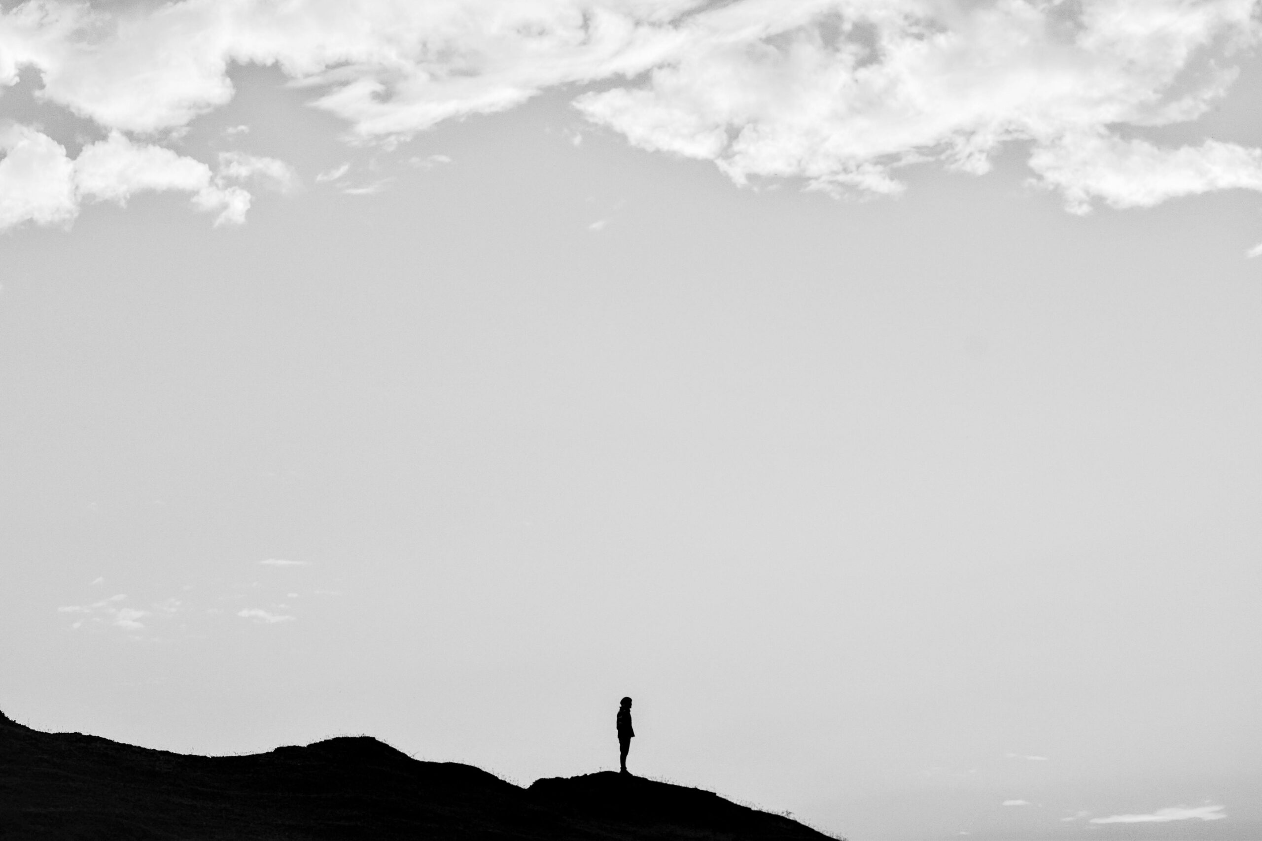 Black and white silhouette of a person standing on a mountain under a cloudy sky.