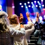 A group of people with raised hands attending a lively worship service inside a church.