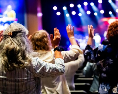A group of people with raised hands attending a lively worship service inside a church.