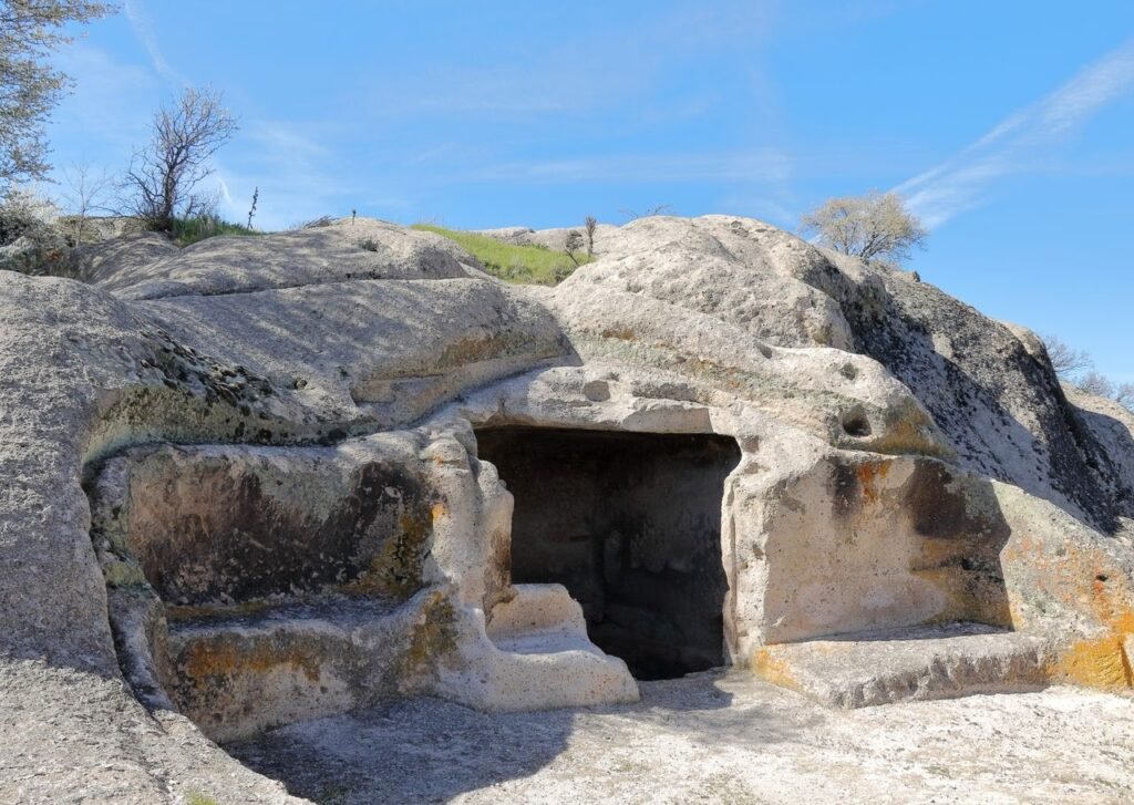 A historic rock-carved cave with natural erosion patterns under a clear blue sky, showcasing ancient architecture.