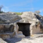 A historic rock-carved cave with natural erosion patterns under a clear blue sky, showcasing ancient architecture.