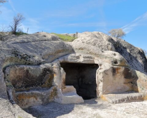 A historic rock-carved cave with natural erosion patterns under a clear blue sky, showcasing ancient architecture.